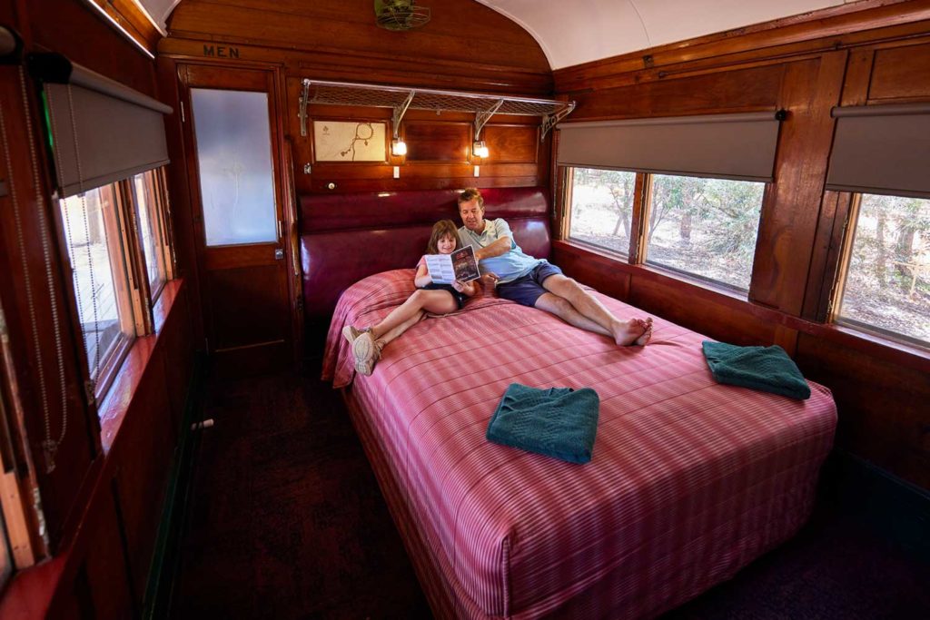 Father and sun on bed in renovated turn of the century railway carriage at Undara Experience